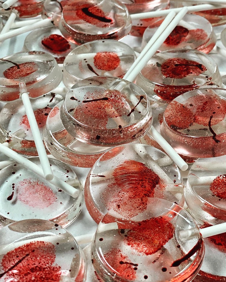 Clear round lollipops with red edible fingerprints and blood spatter on white sticks.